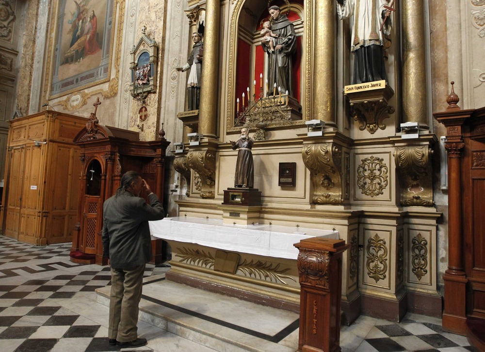 Man stands in front of side altar in ornate church. 