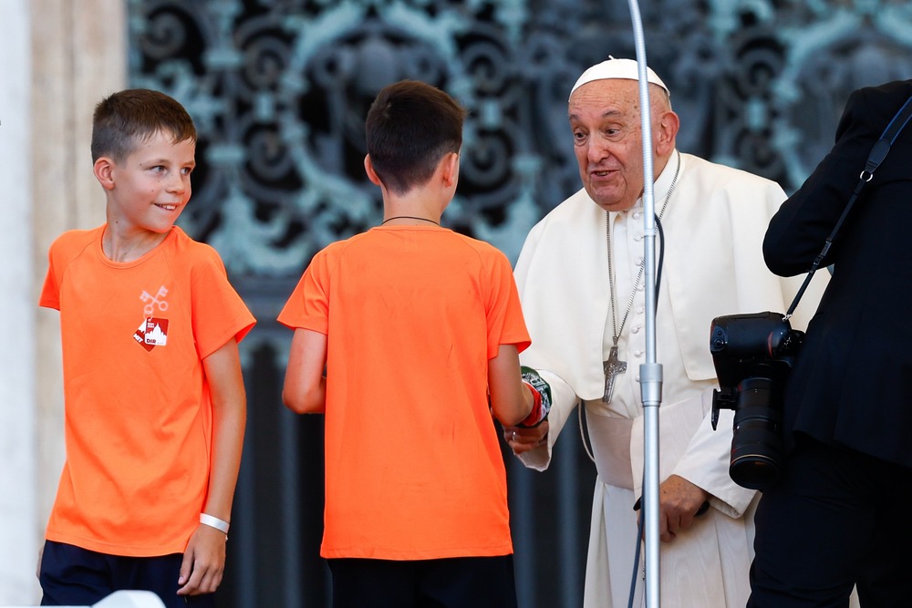 Pope Francis, standing, bends to shake the hand of a young altar server. 