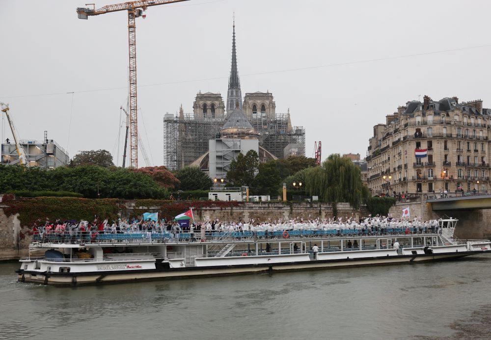 An athlete boat on the Seine River passes in front of the Notre Dame Cathedral July 26, 2024, during the opening ceremony of the Olympic Games in Paris. 