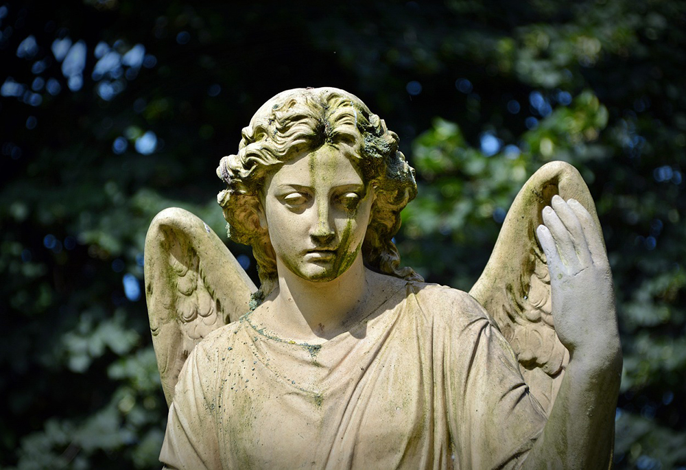 A photo illustration shows a stone sculpture of an angel, with its face discolored in an outdoor setting. (Pixabay/Bernswaelz)