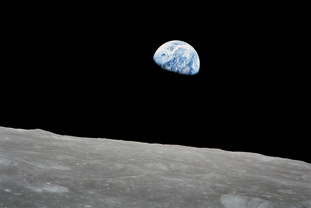 The rising Earth is about five degrees above the lunar horizon in this telephoto view taken from the Apollo 8 spacecraft near 110 degrees east longitude. Astronaut Bill Anders took the photo on the morning of Dec. 24, 1968. The South Pole is in the white area near the left end of the terminator. North and South America are under the clouds. (NASA)