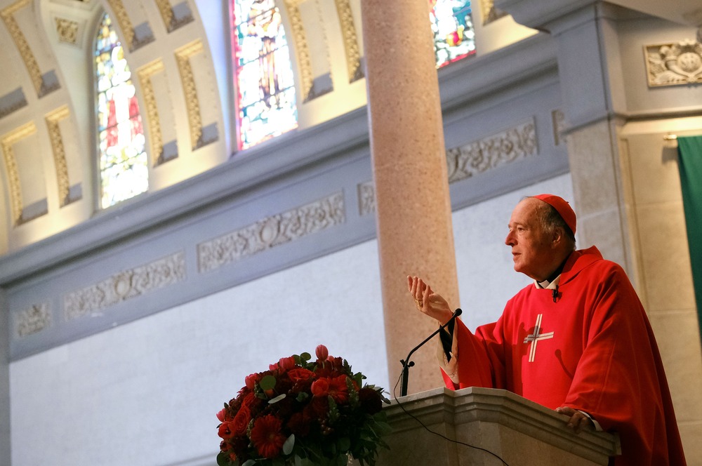 McElroy preaches from pulpit, the ceiling of the sanctuary fills the frame around him. 