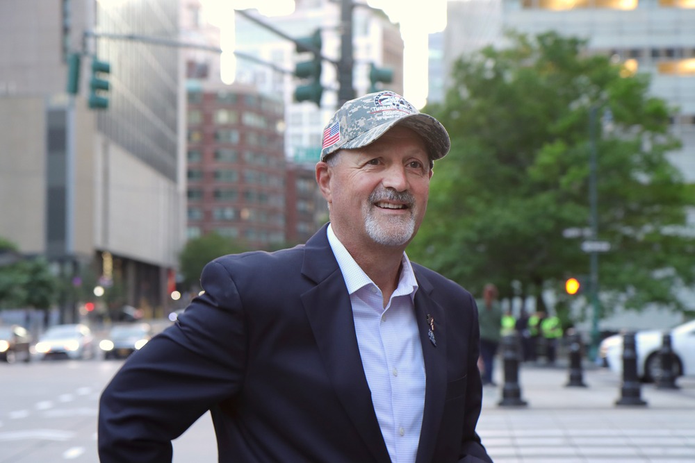 Siller stands in New York City, wearing a suit jacket and ballcap. 