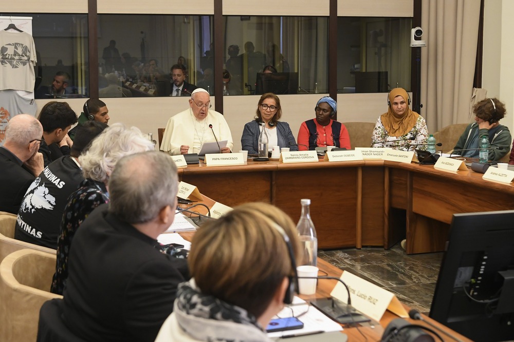 Pope sits at head of U-shaped table reading remarks.