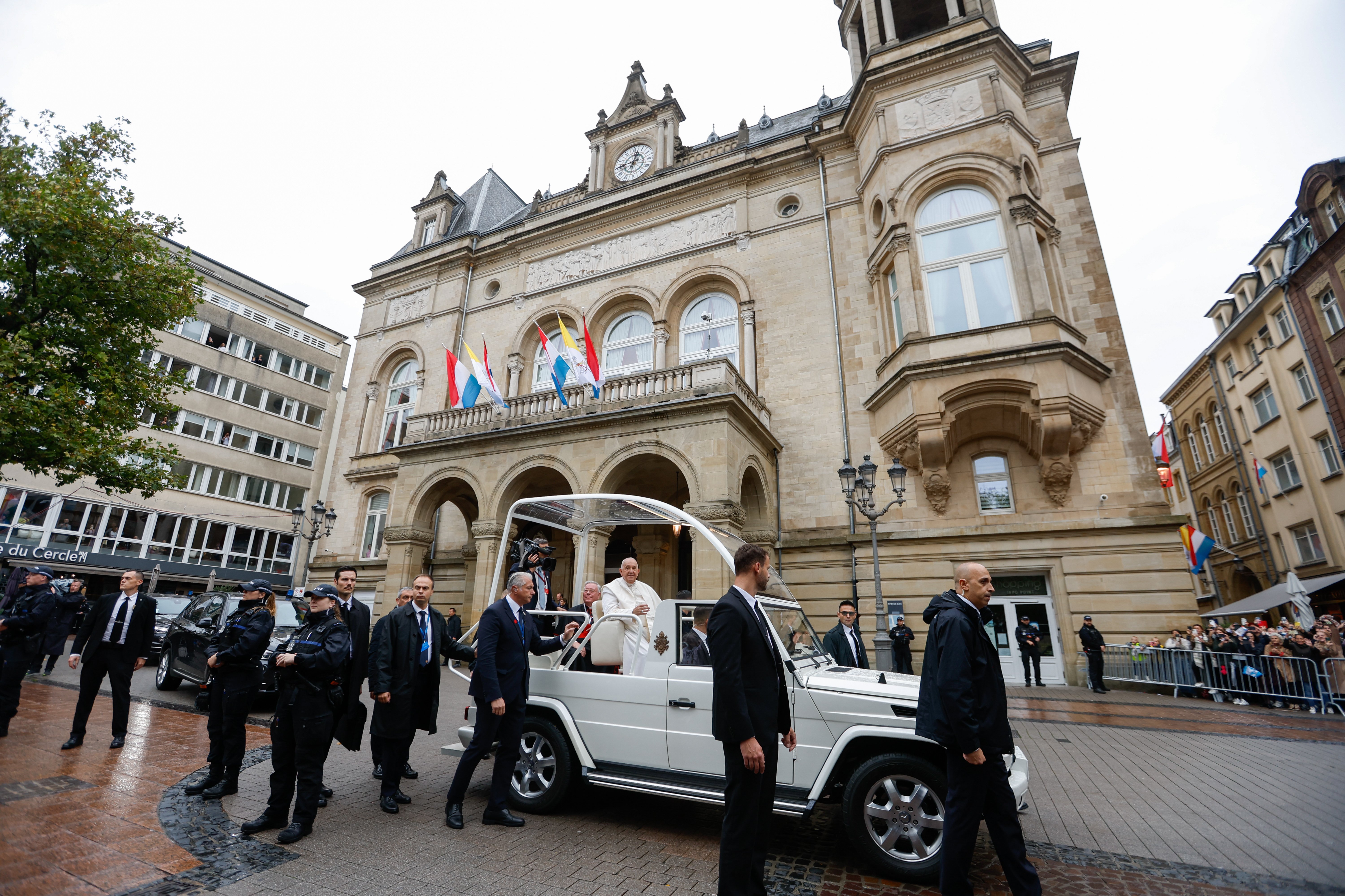 Pope Francis greets people gathered on the streets of Luxembourg to see him pass by in the popemobile Sept. 26, 2024. (CNS photo/Lola Gomez) 		