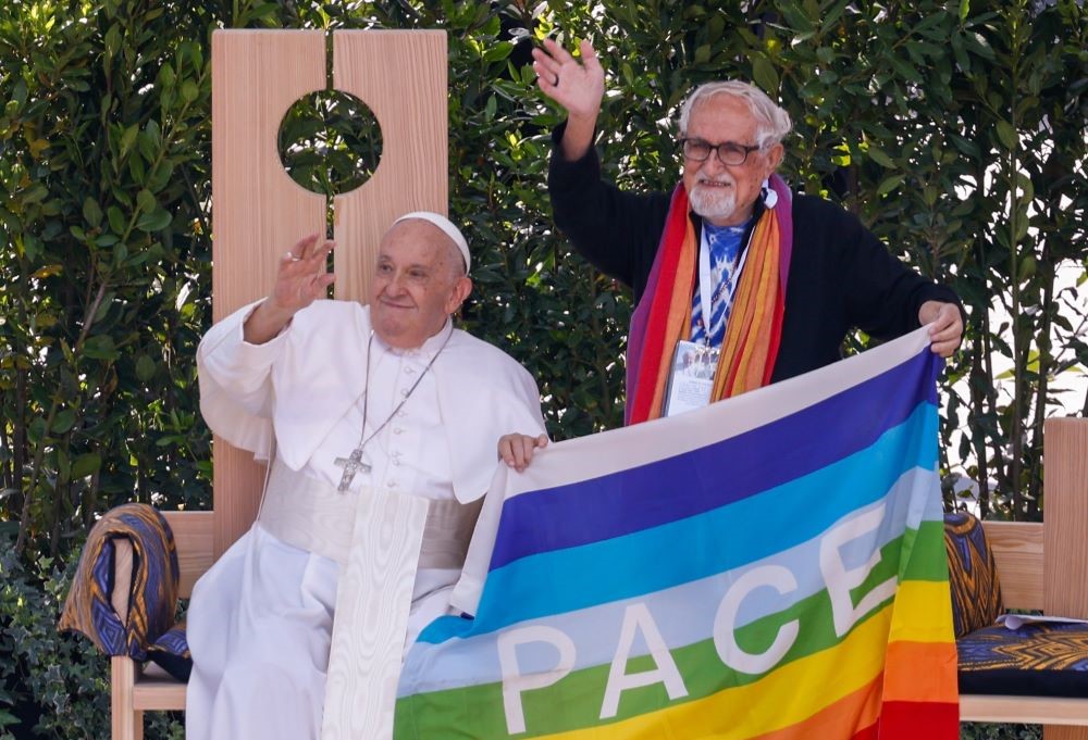 Pope Francis waves to and holds a flag that says, "Pace." 