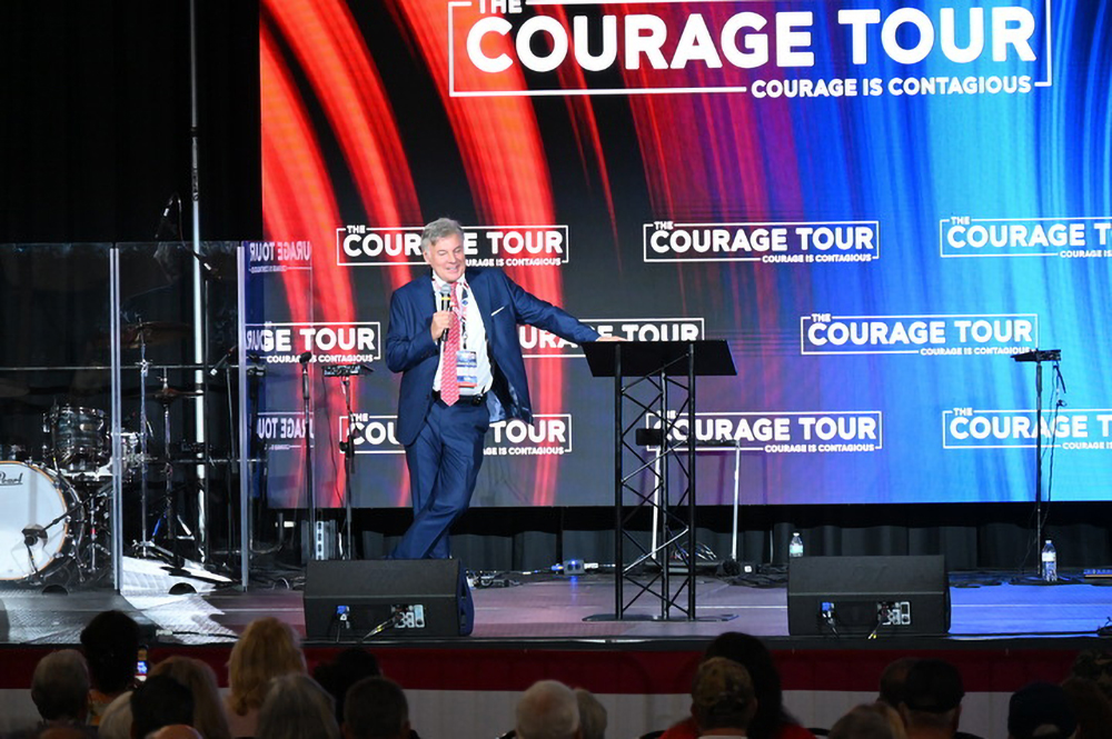 Wallnau speaks on stage, leaning against lectern. 