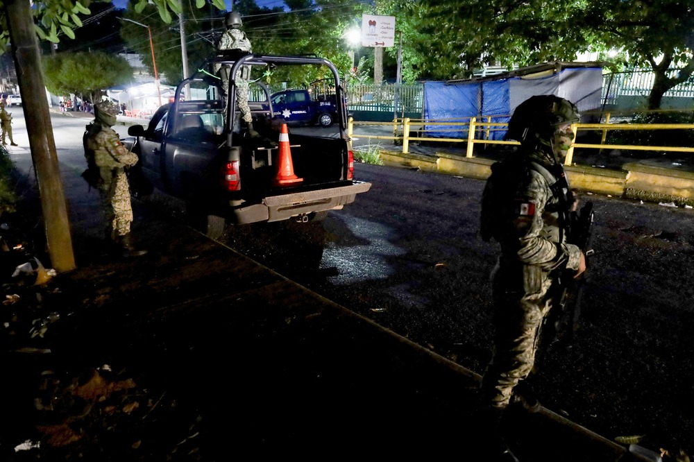 Two armed soldiers stand in a street at night.