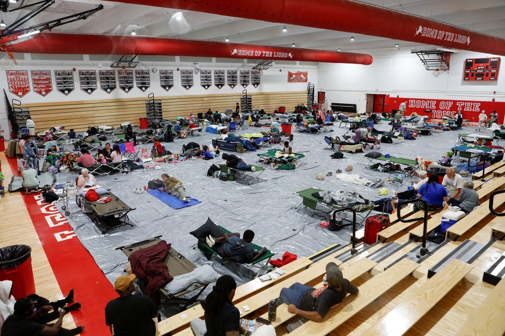 Overhead view of people sleeping on mats and cots in large gym.