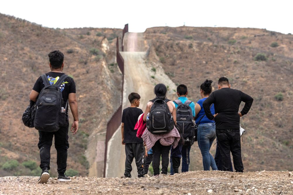 The border wall is seen in the background as migrants from South and Central America look to surrender to immigration officials after crossing into the United States from Mexico in Ruby, Ariz., June 24. 