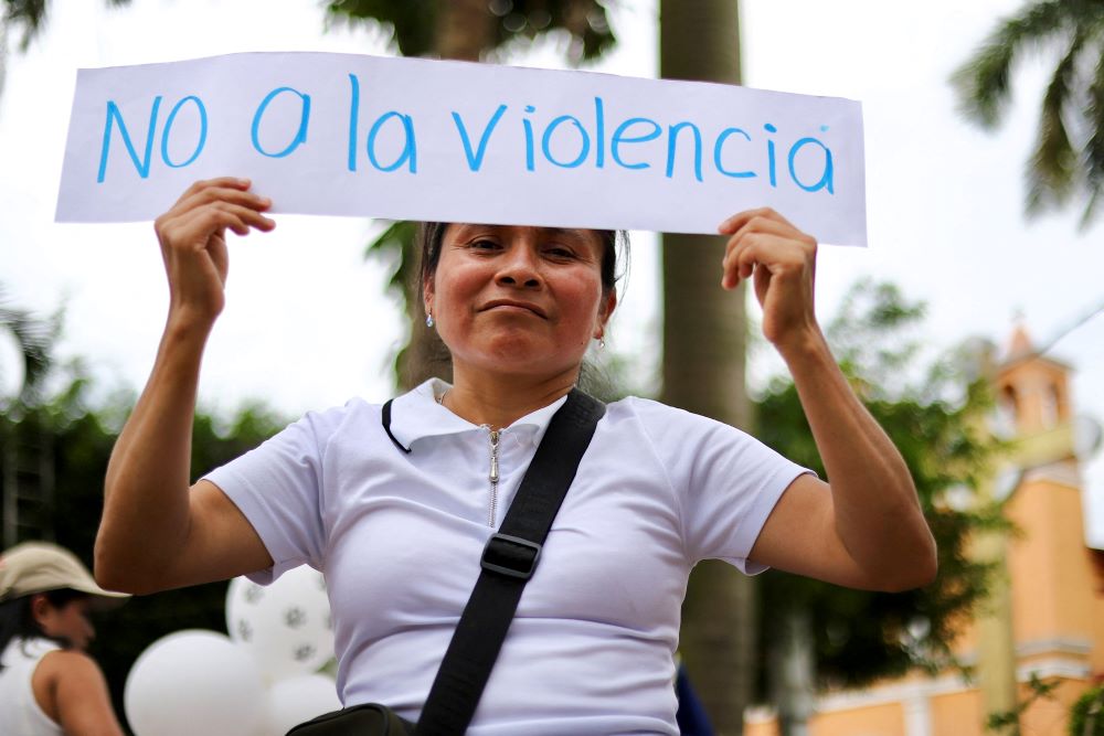 A woman holds a sign reading, "No To Violence."