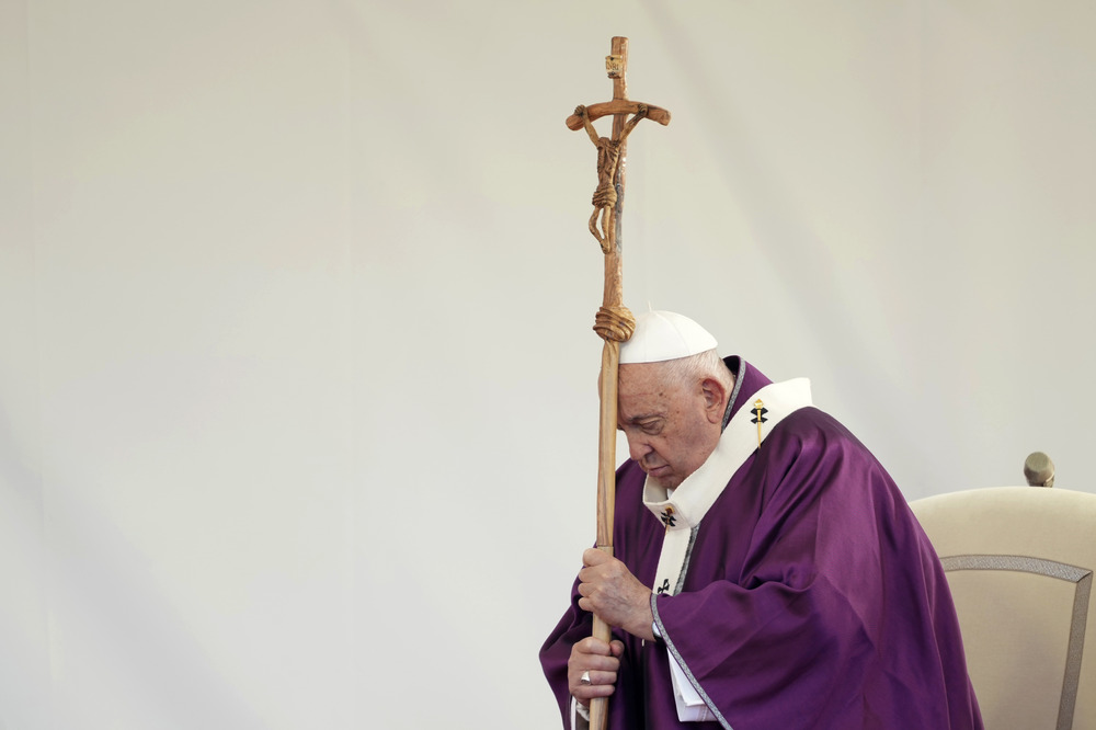 Pope, vested in penitential purple, stands, and leans head on processional cruxifix.