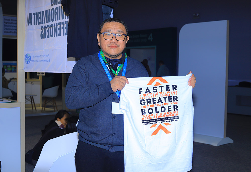 Rodne Rodiño Galicha, the executive director of Living Laudato Si' Philippines, holds a printed t-shirt with a climate change message on the background at COP 29 in Baku, Azerbaijan, on Nov. 11-22. (NCR photo/Doreen Ajiambo)