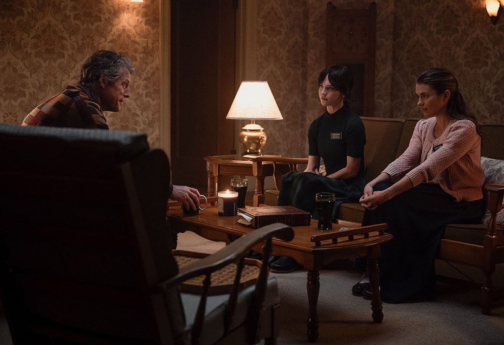 In "Heretic," two Mormon missionaries (Sophie Thatcher, center, and Chloe East, right), are invited into the home of Mr. Reed (Hugh Grant). A guise of desire to learn more about the Church of Jesus Christ of Latter-day Saints hides Reed's sinister plan. (A24 Press)