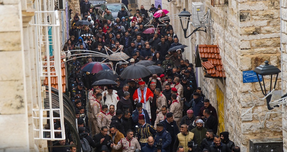 Narrow, antiquated street depicted aerially, and filled with clergy and faithful.