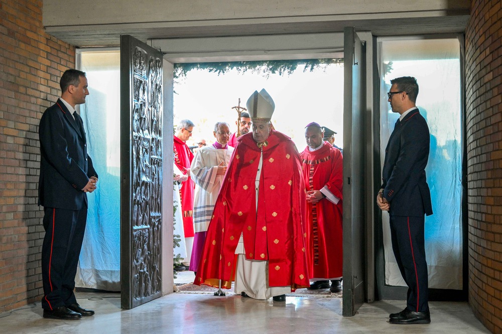 The pope, vested, walks through open double doors. 