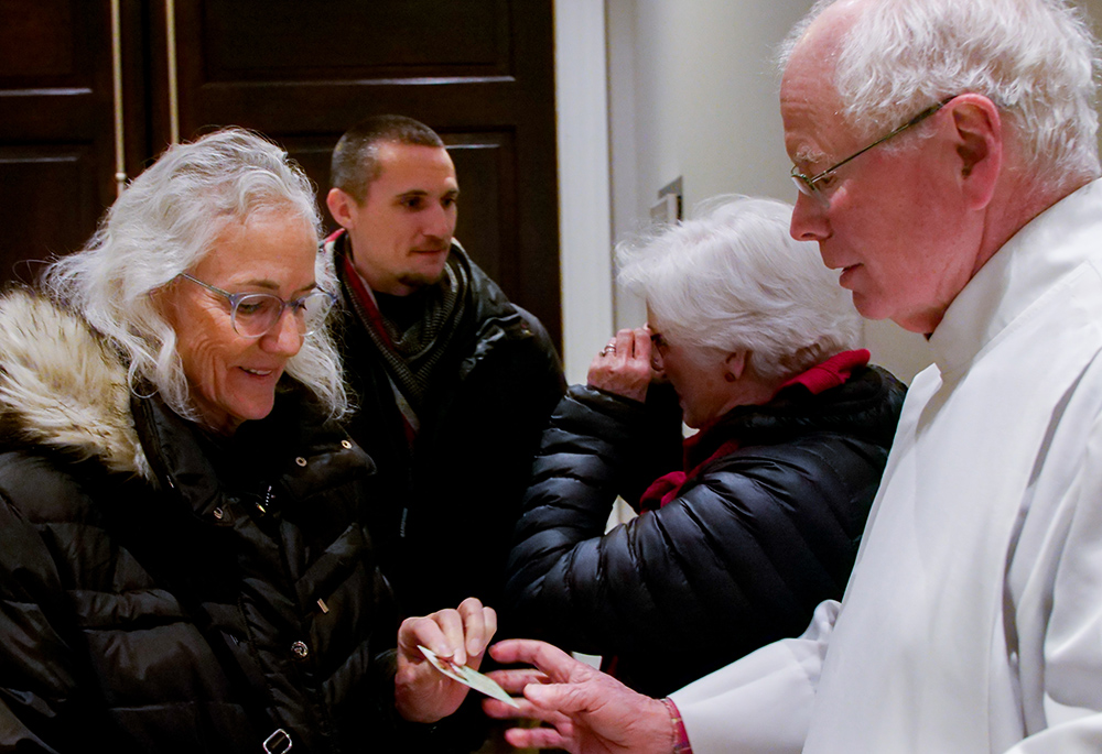 Debra Tice gives Jesuit Fr. Kevin Gillespie a magnet with a picture of her son Austin, before a Vigil Mass Dec. 15 at Holy Trinity Church. Her son Simon Robert is pictured behind her. (NCR photo/Anthony Peltier)