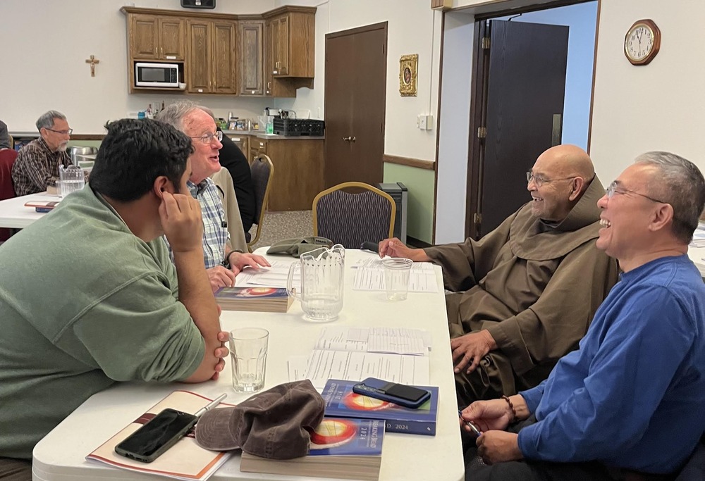 Four men sit around  table laughing and talking. 