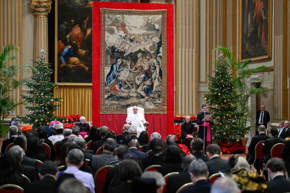 Pope sits on raised dais in front of tapestry facing diplomats.