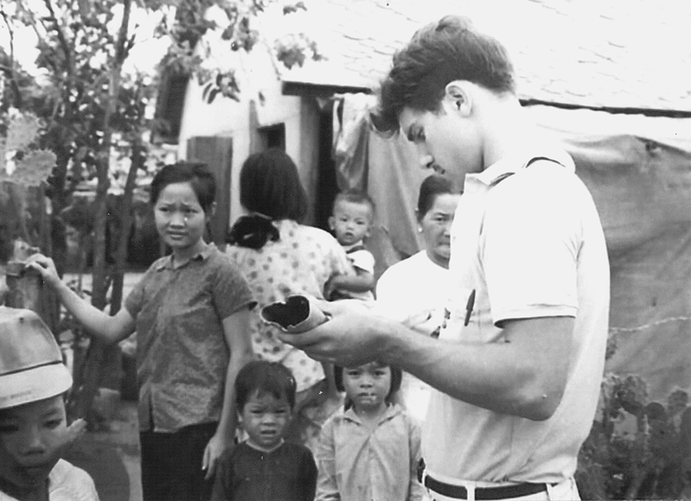 Tom Fox inspects a mortar shell that landed near his home circa 1966 in Tuy Hoa, Vietnam, while local Vietnamese residents look on. (Courtesy of Thomas C. Fox)