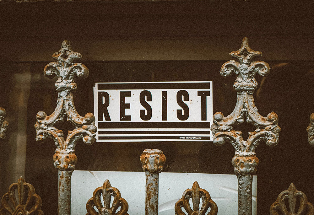 Sign behind a gate says, "RESIST" (Unsplash/Jon Tyson)