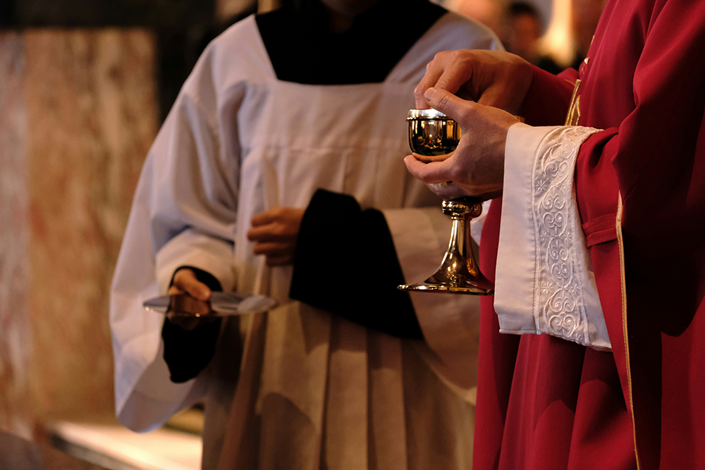 Two priests, one holding a cup and the other holding Communion wafers (Unsplash/Julia Michelle)