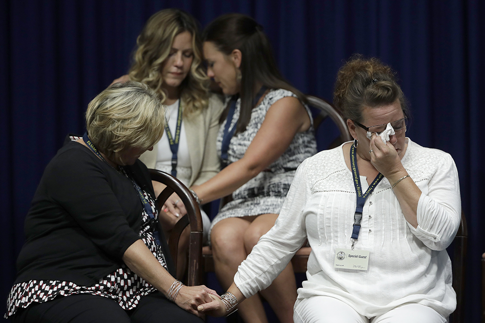 Four women sit while dabbing tears and holding hands.