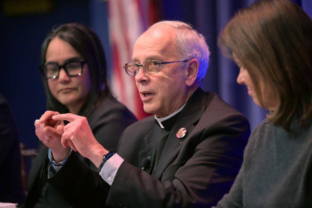 Seitz shown with two others sitting on panel and speaking.