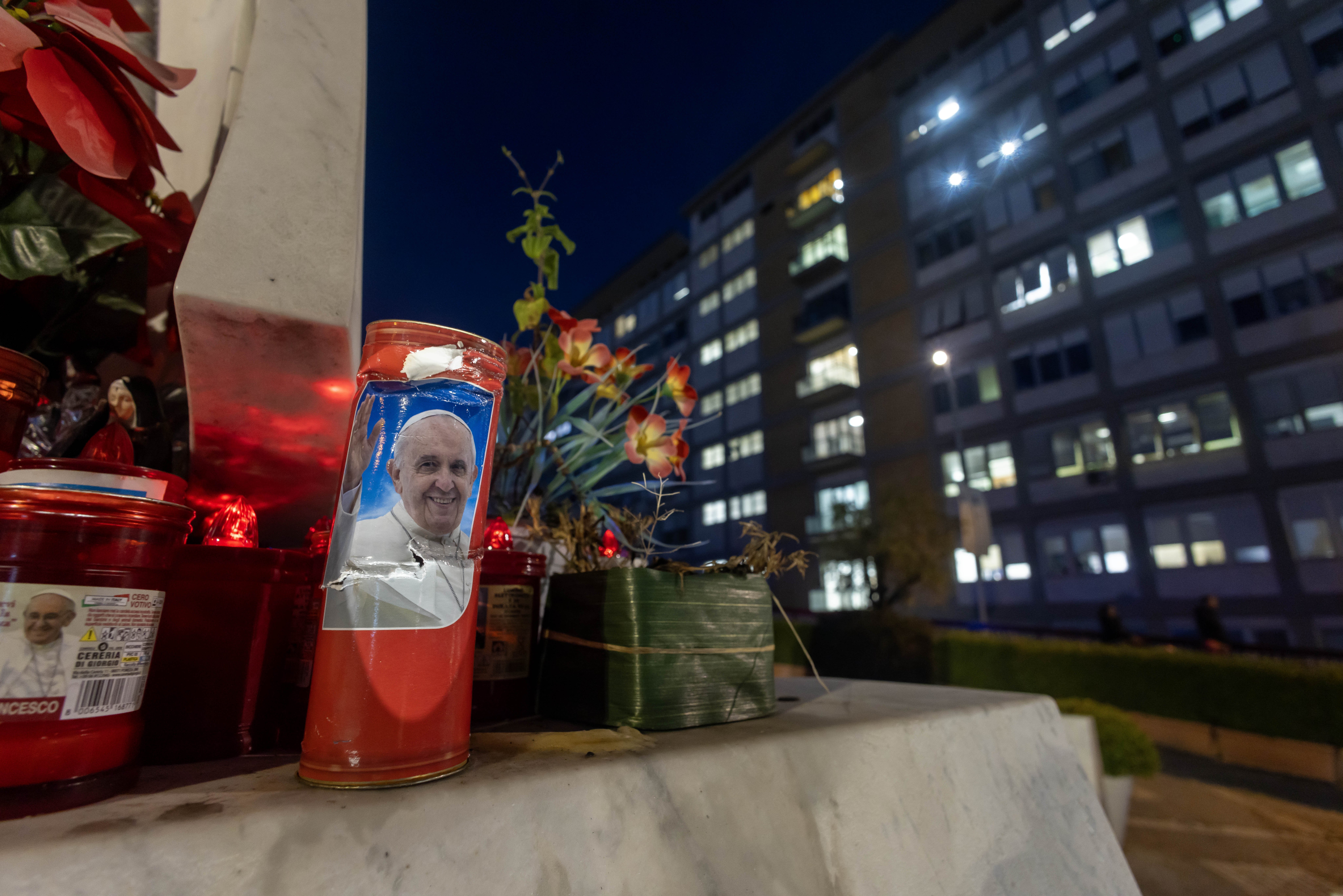 Votive candles, including some bearing a photo of Pope Francis, are seen on the base of a statue of St. John Paul II outside Rome's Gemelli hospital on Feb. 15. (CNS/Pablo Esparza)