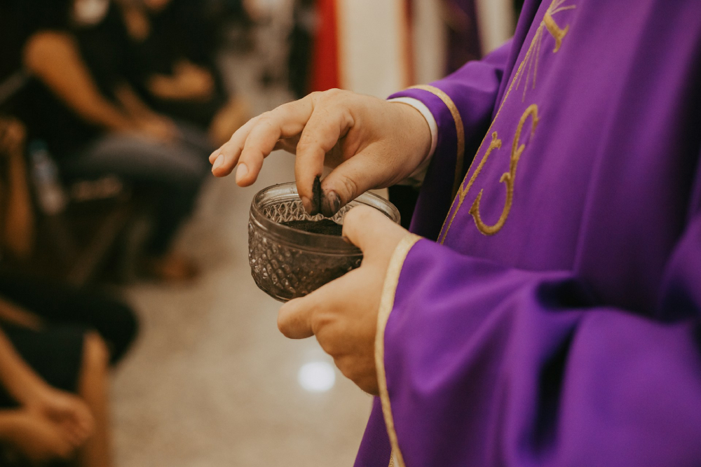 Someone takes a pinch of ashes from a bowl full of ashes at an Ash Wednesday Mass, the first day of Lent.