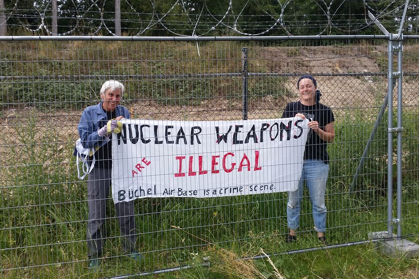 Eighty-one-year-old activist grandma Susan Crane (left), a Catholic Worker from Redwood City, California, takes a banner with her anti-nuclear proliferation message inside Büchel Air Force Base in Büchel, Germany. The banner reads, "NUCLEAR WEAPONS ARE ILLEGAL; Büchel Air Base is a crime scene." (Courtesy of Susan Crane)