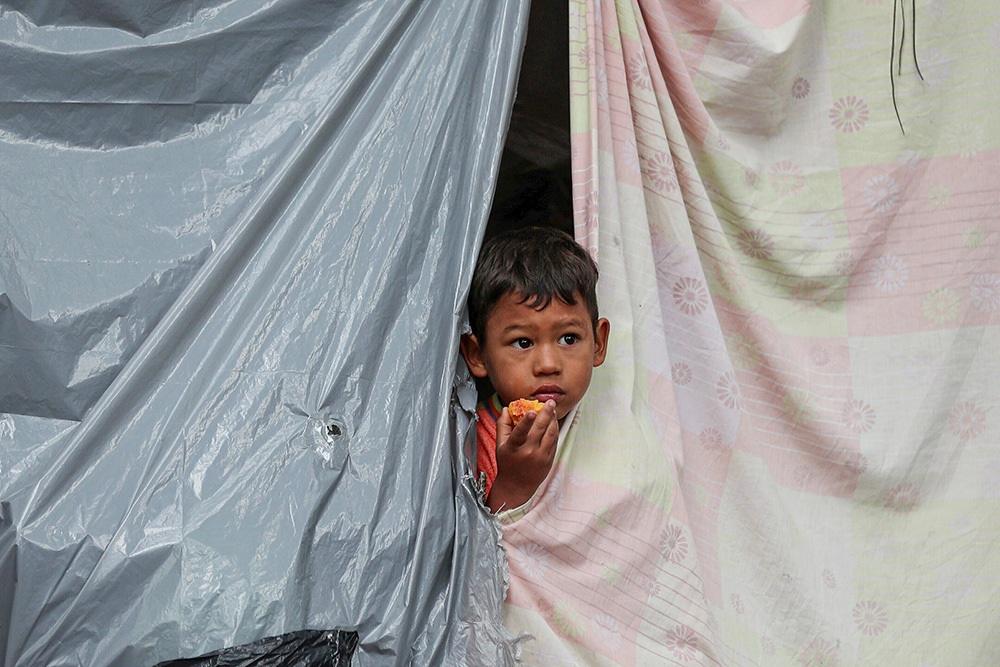 The child of a Venezuelan migrant peers from a tent at an encampment set up by migrants in a park near the main bus terminal in Bogotá, Colombia, June 3, 2020. Staff layoffs following the Trump administration's freeze on foreign aid in early 2025 have hit hardest so far in Colombia, where Jesuit Refugee Service assists Venezuelan refugees and others in accessing asylum to stay in that country. (AP Photo/Fernando Vergara)