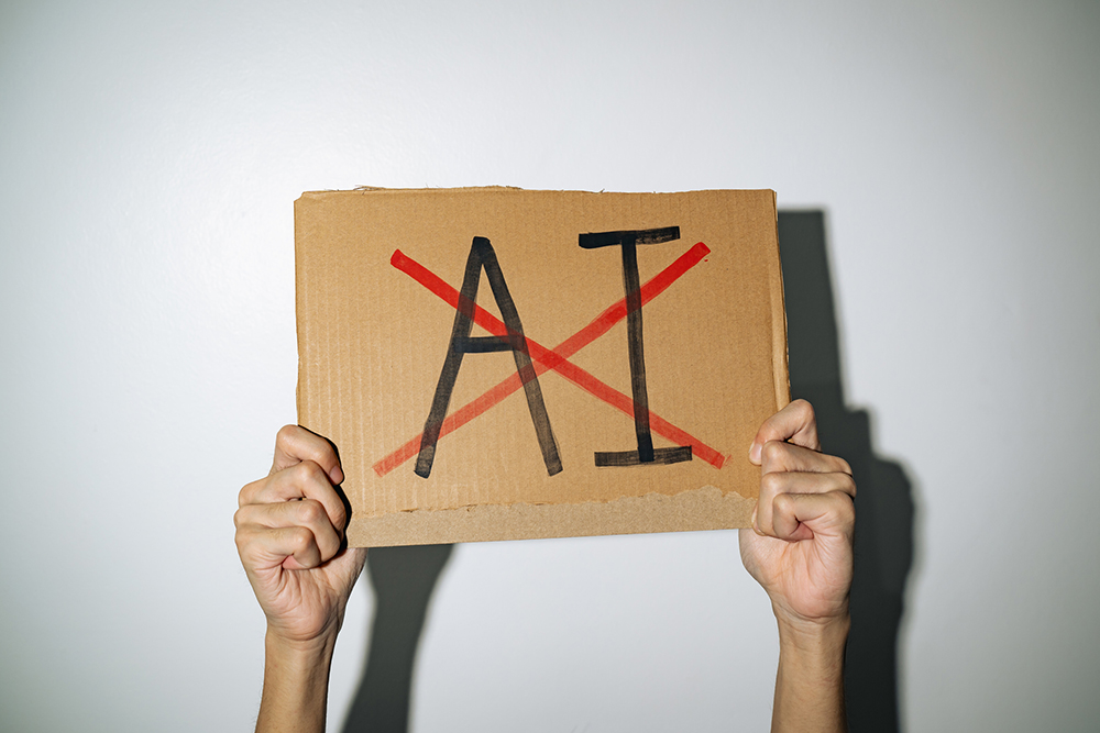 Hands holding a cardboard sign with the letters AI crossed out (Dreamstime/Wachiwit)