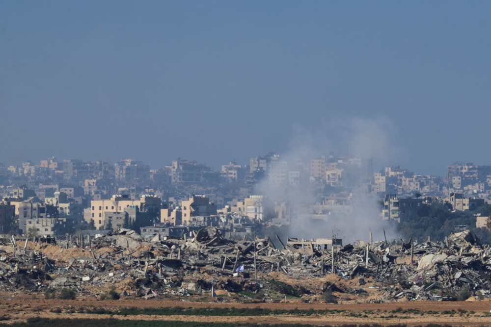 An Israeli flag flies next to the rubble of destroyed buildings Dec. 26, 2023, as smoke rises in the Gaza Strip, as seen from southern Israel.