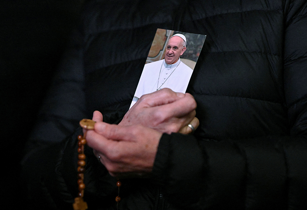 A person holds a picture of Pope Francis and a rosary during a prayer service in St. Peter's Square at the Vatican on Feb. 25, as Pope Francis continued his hospitalization. (OSV News/Reuters/Dylan Martinez)