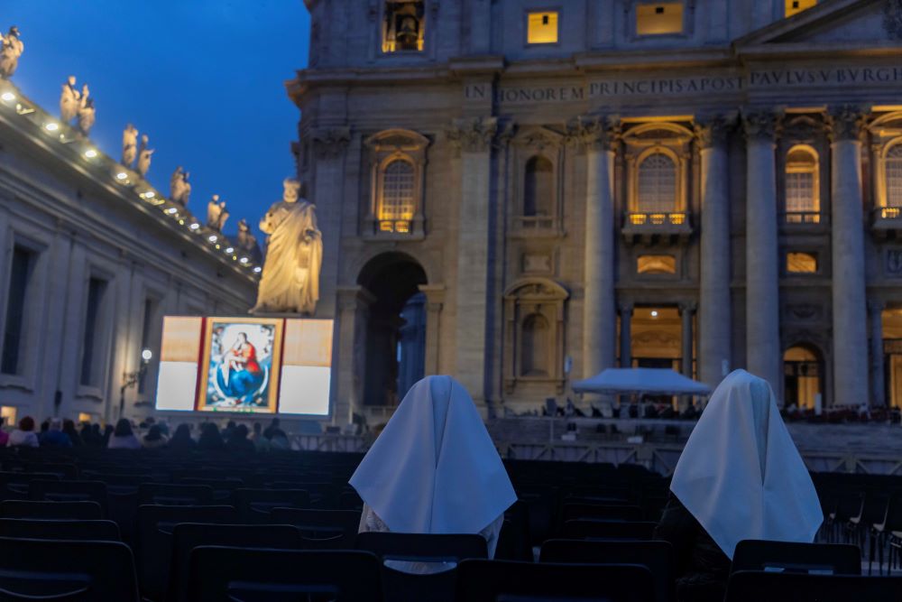 Nuns pray rosary in St. Peter's Square with large video scree.