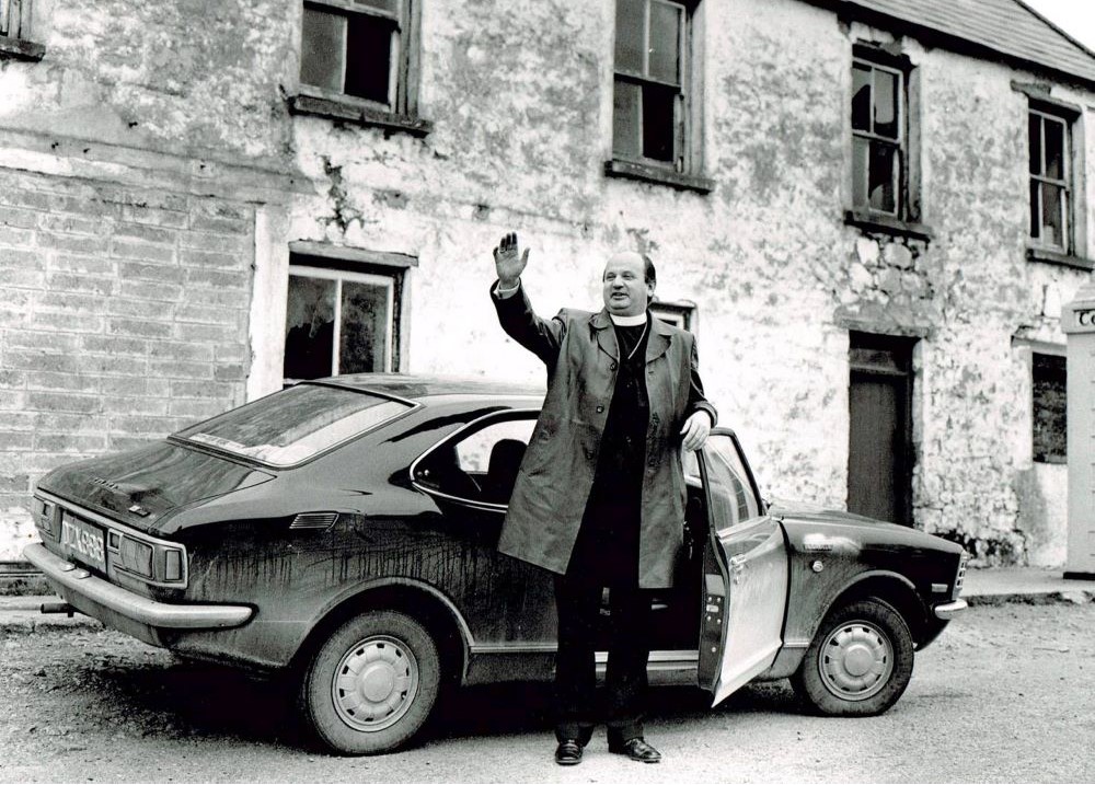 Priest stands by car and waves.