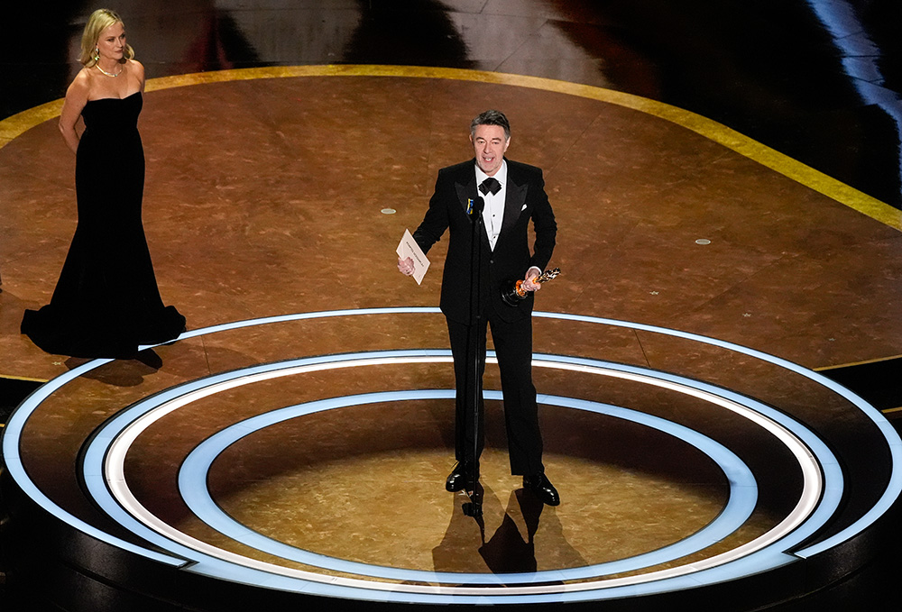 Peter Straughan accepts the award for Best Adapted Screenplay for "Conclave" during the Oscars on Sunday, March 2, 2025, at the Dolby Theatre in Los Angeles. Amy Poehler looks on from left. (AP/Chris Pizzello)