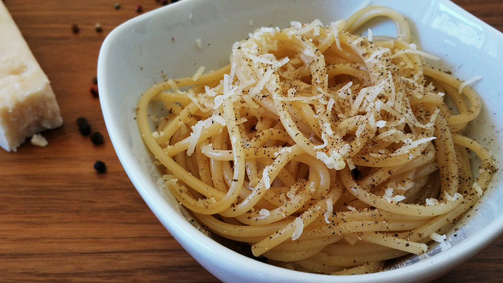 Cacio e pepe in a white bowl with ingredients on a wooden table (Wikimedia Commons/Popo le Chien)