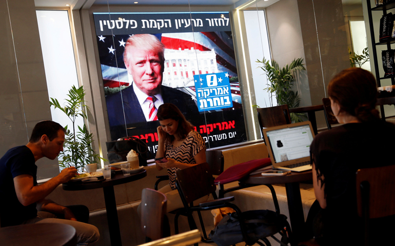 People dine at a Tel Aviv coffee shop Nov. 9 as an image of President-elect Donald Trump is displayed on a monitor. (CNS/Baz Ratner, Reuters)