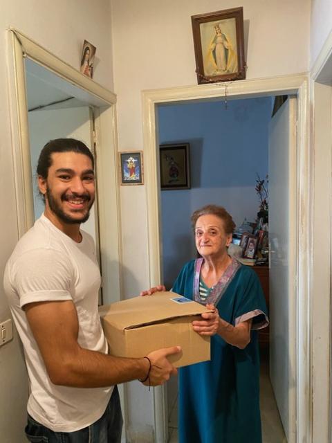 Young man, holding package, smiles alongside elderly woman who stands in her home. 