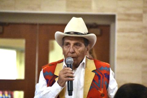 Archambault, wearing patterned vest and cowboy hat, speaks into microphone. 