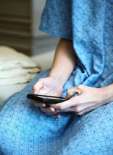 A closeup photo illustration shows a patient in a gown sitting on what appears to be a hospital bed. The patient is using a smartphone. (Unsplash/Alexander Grey)