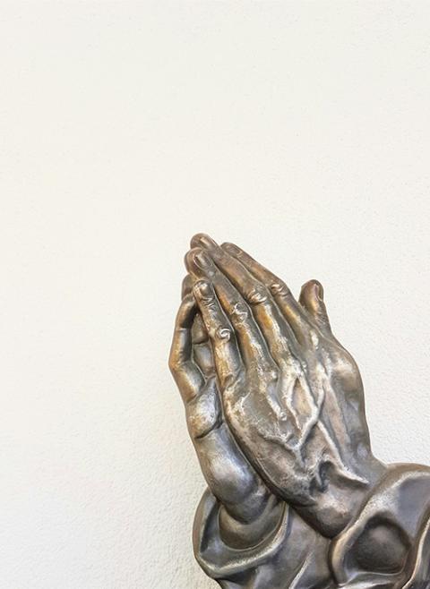 A photo illustration features a statue's hands folded in prayer. (Unsplash/Deb Dowd)