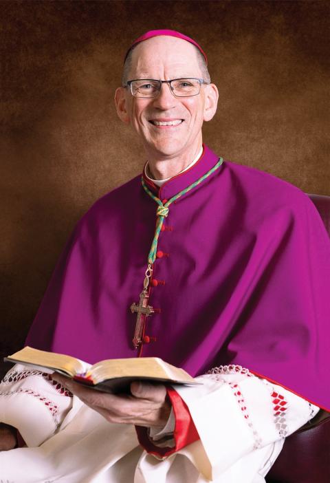 Formal portrait of the bishop in choir dress smiling. 