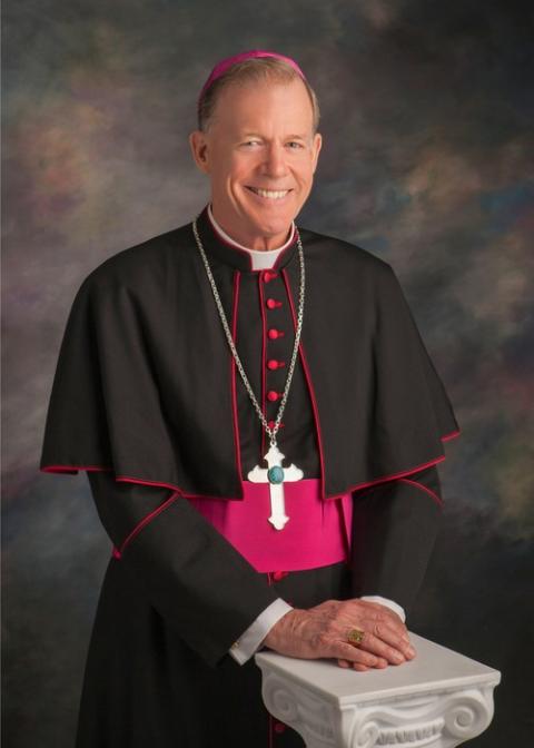 Formal portrait of Wester, standing in bishop's choir dress, hands folded and resting on short ionic column.