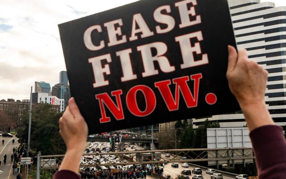 A protester holds a sign calling for a cease-fire to the Israel-Hamas war as others block Interstate 5 northbound on Jan. 6 in downtown Seattle. (AP/Lindsey Wasson)