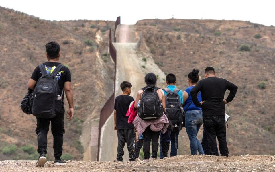 The border wall is seen in the background as migrants from South and Central America look to surrender to immigration officials after crossing into the United States from Mexico in Ruby, Ariz., June 24. (OSV News/Reuters/Adrees Latif)