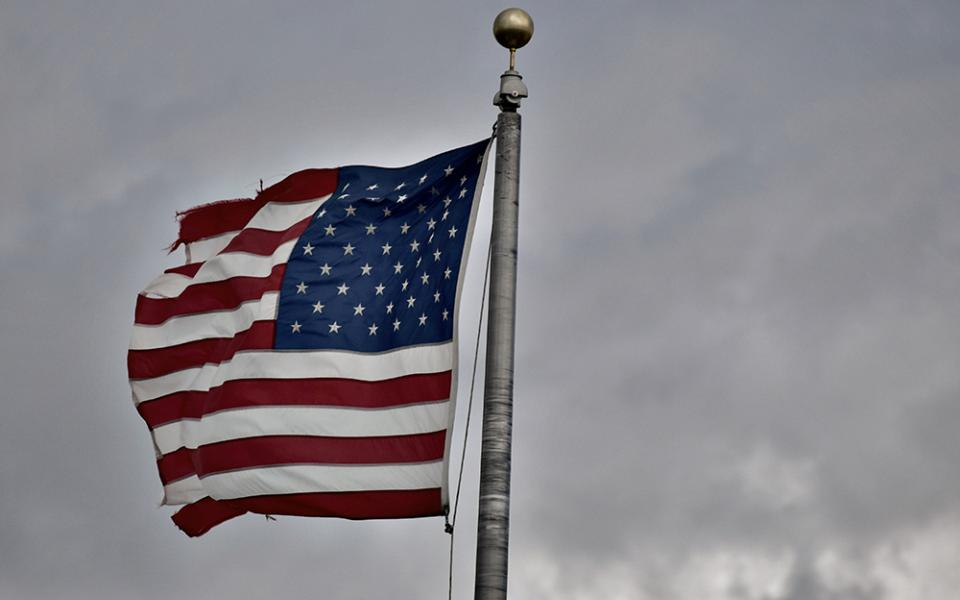 Tattered American flag against cloudy sky (Unsplash/Kevin Luke)