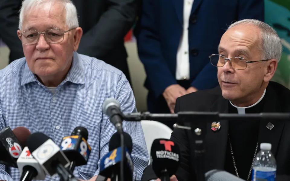 The two men sit side by side in front of microphones, Seitz wears black clerics.